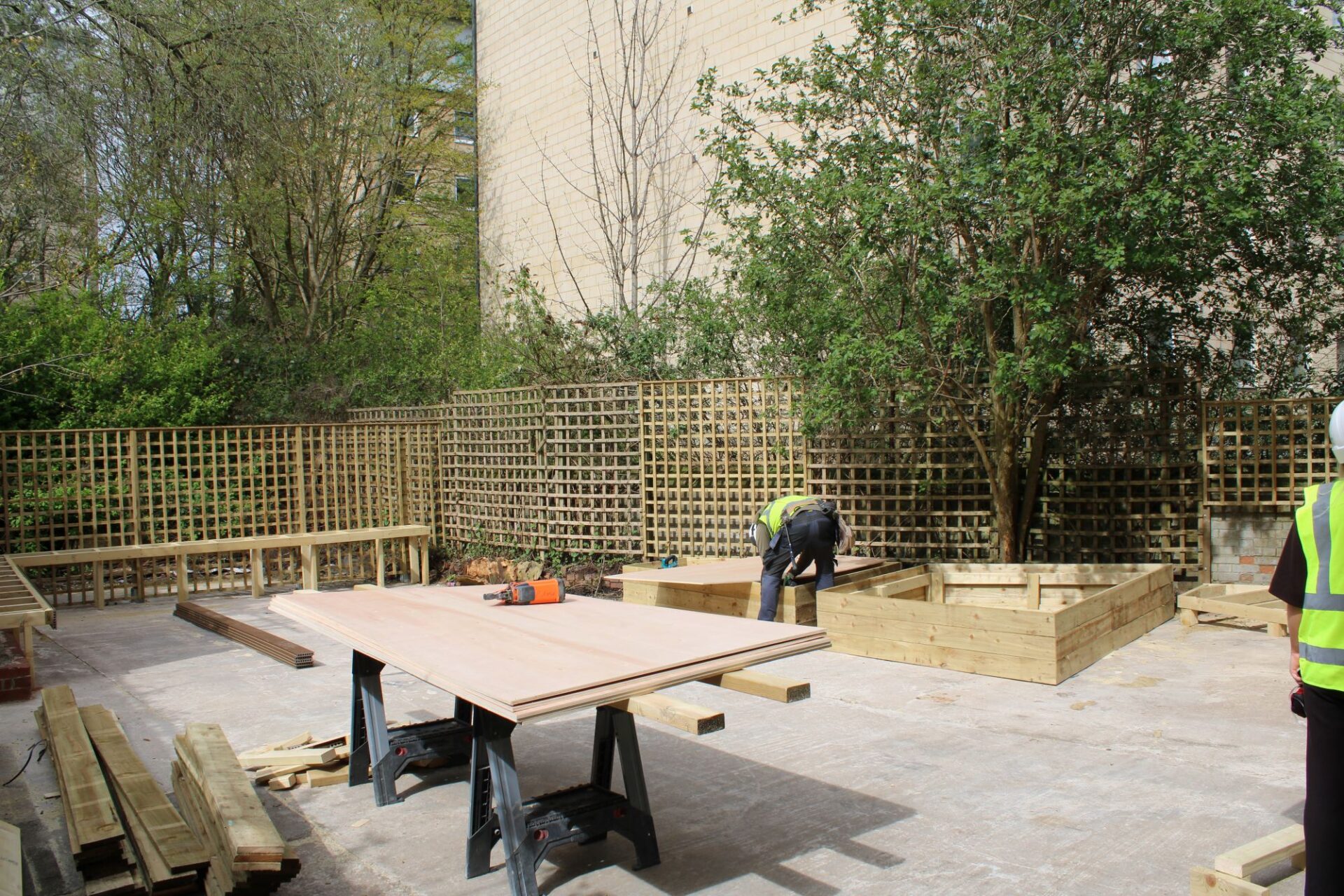 A man bends over while building a raised flower bed in the sunshine.