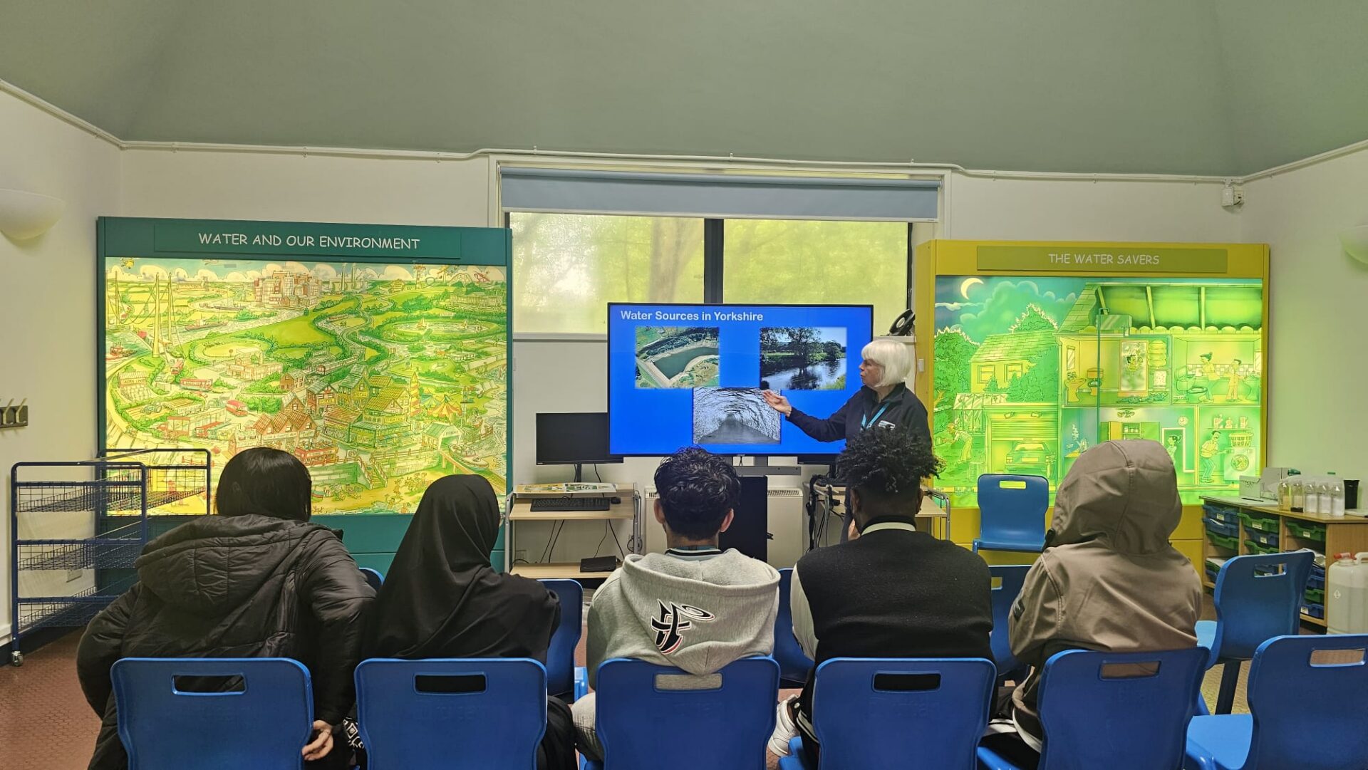 A group of 3 men and 2 women sit looking towards a screen in a classroom showing water sources in Yorkshire.