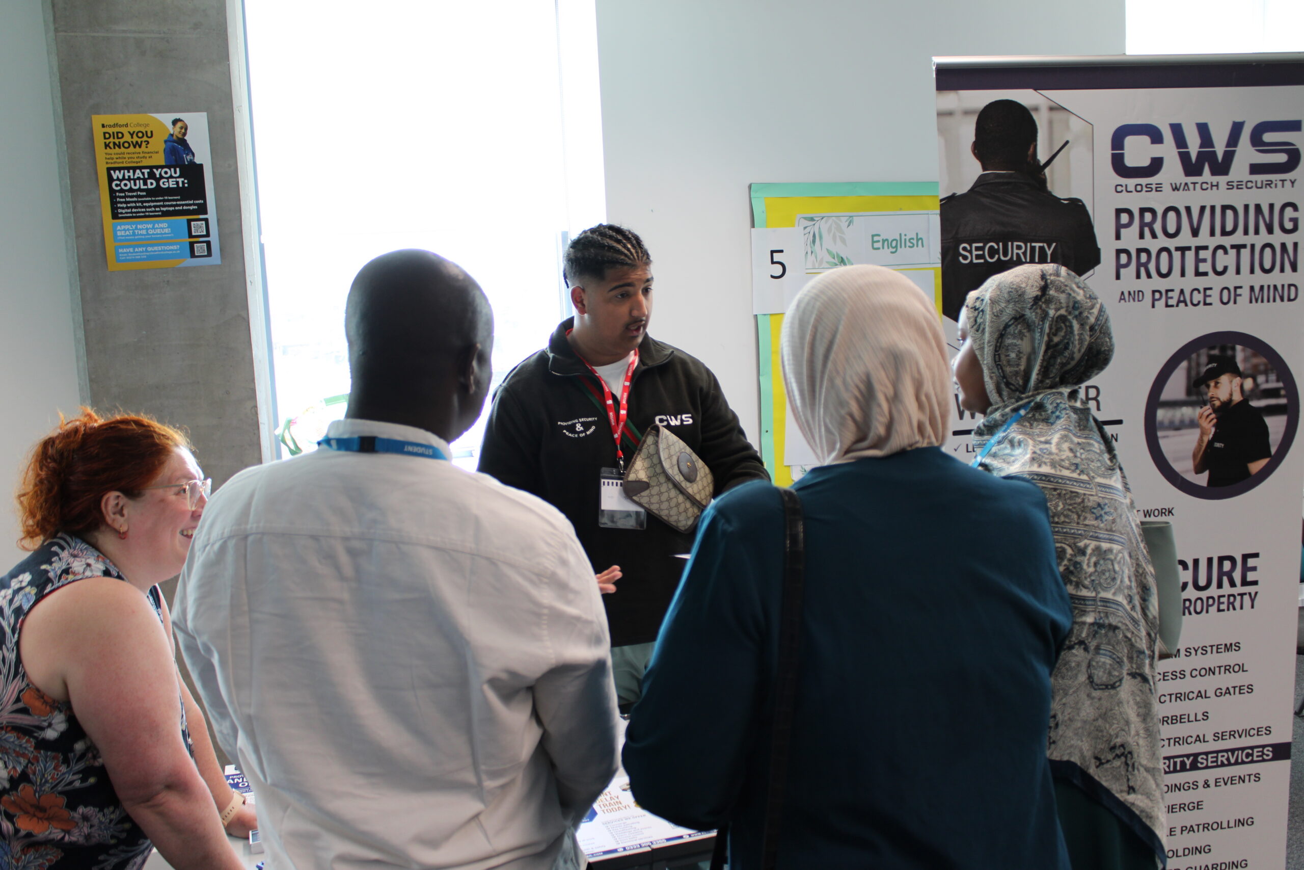A group of people stand in front of a Close Watch Security table and display talking together.