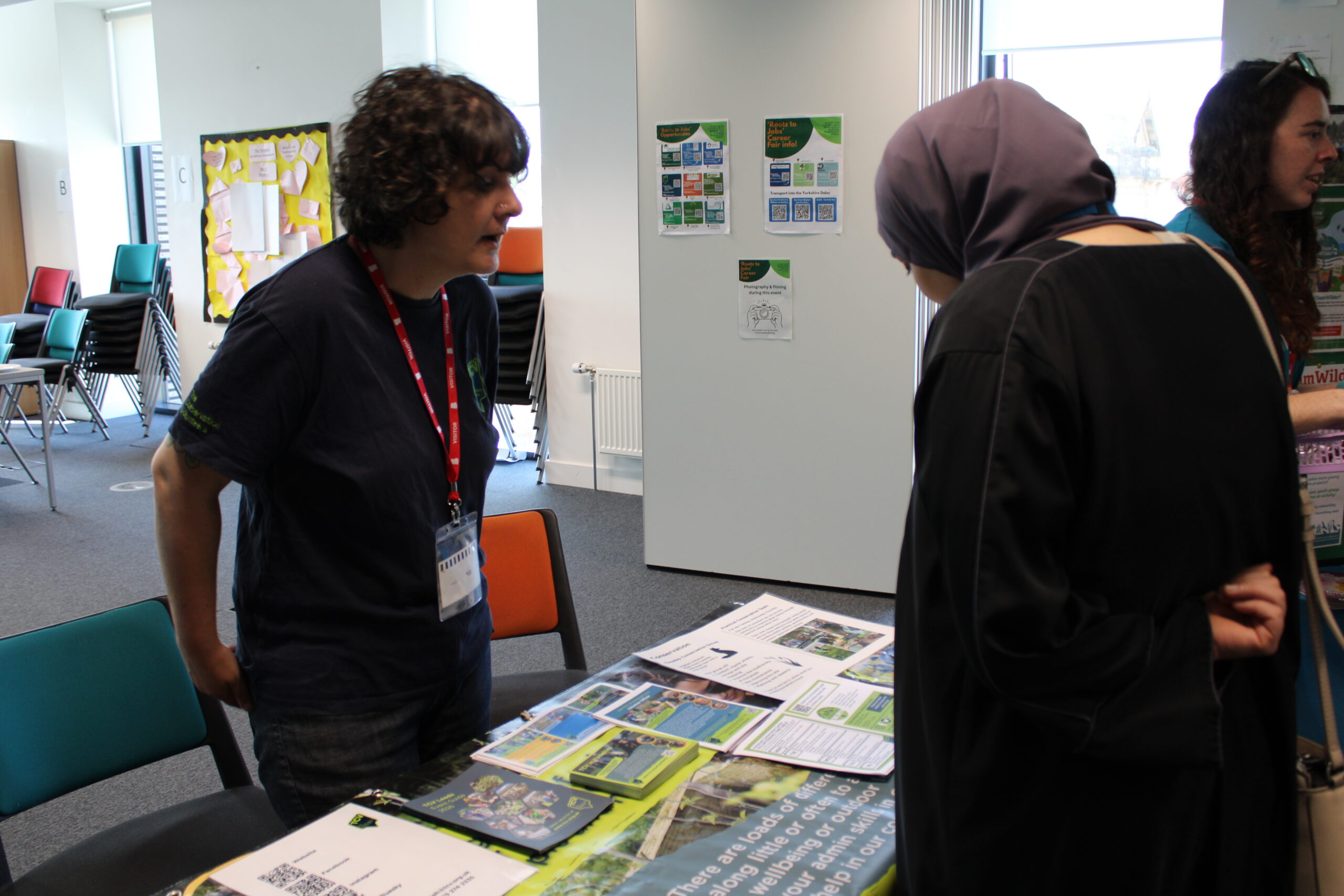 An adult learner speaks with a visitor from the Conservation Volunteers about an information leaflet they are looking at.