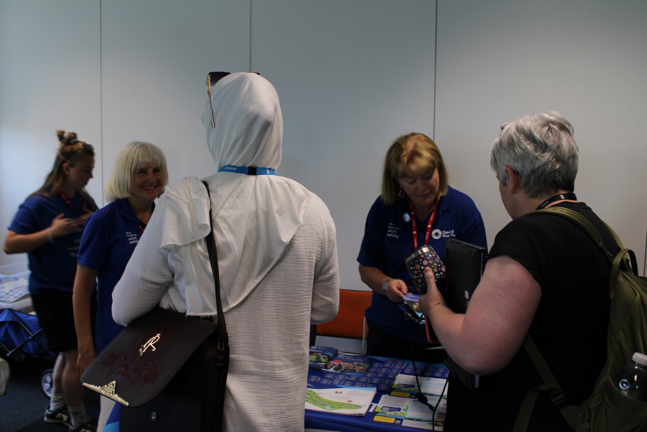 A group of people stand in front of a table and display talking together.