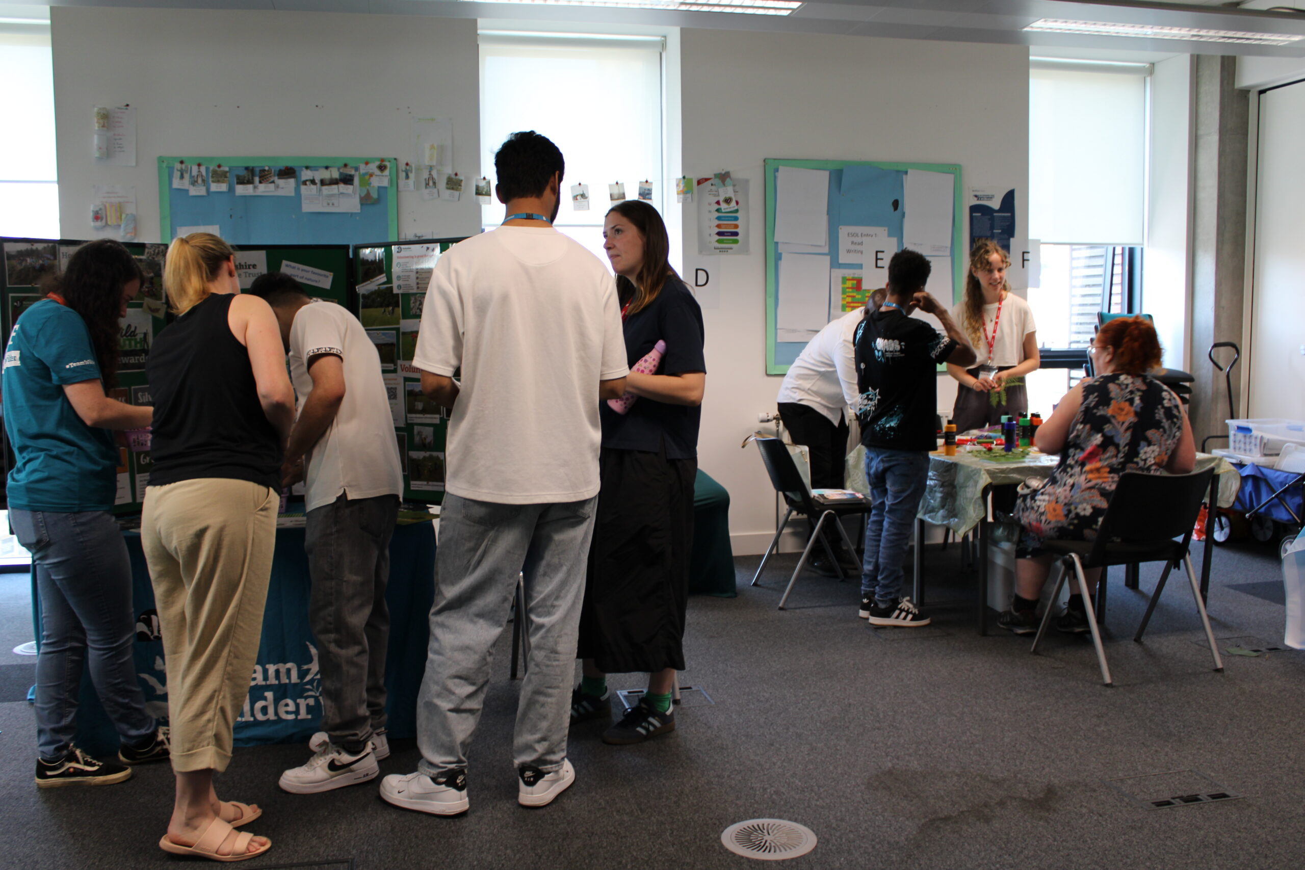 Two groups of adult students stand talking to visitors at tables with displays and activities.