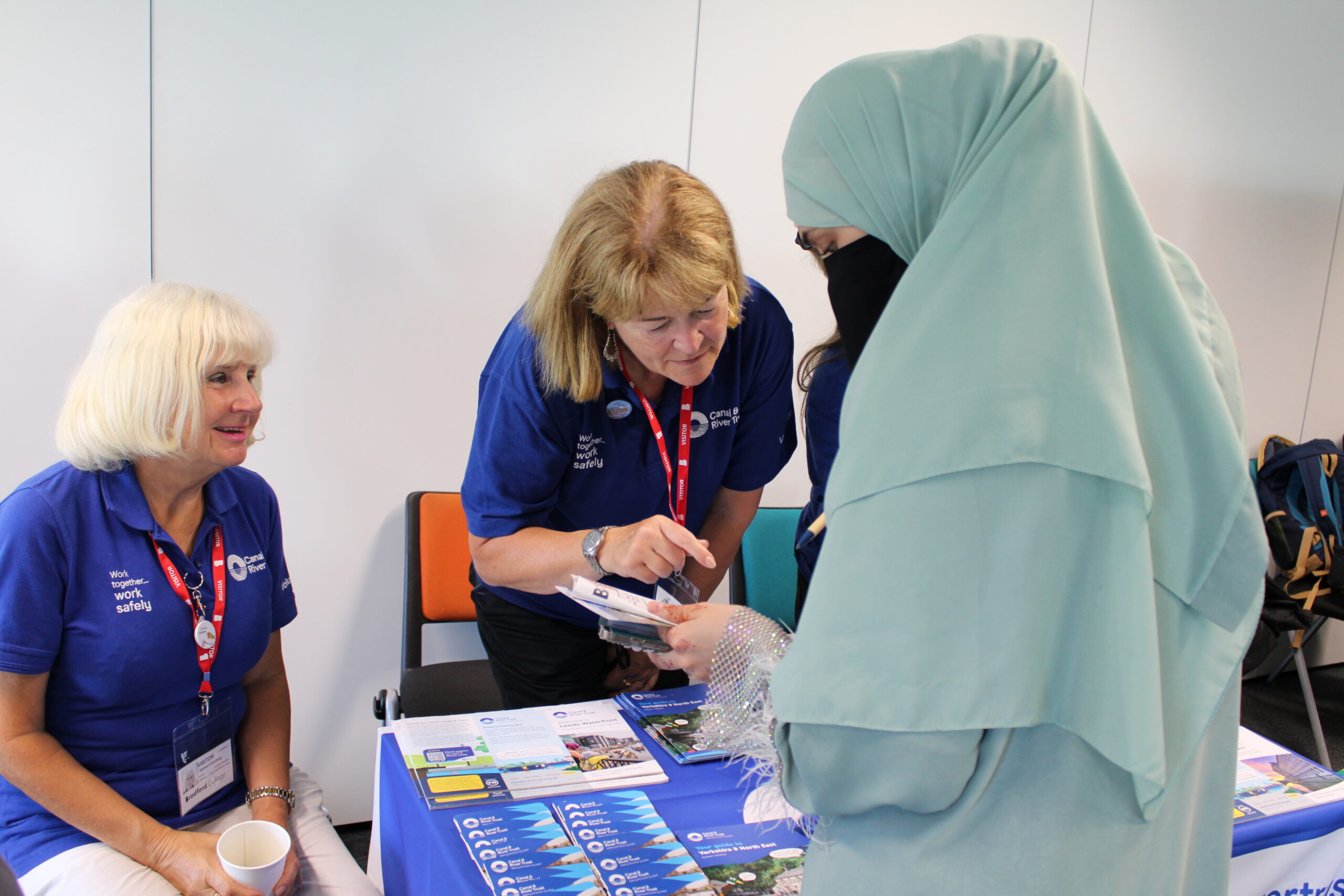 An adult learner and a visitor from the Canal and River Trust talk about volunteering while pointing at a leaflet.