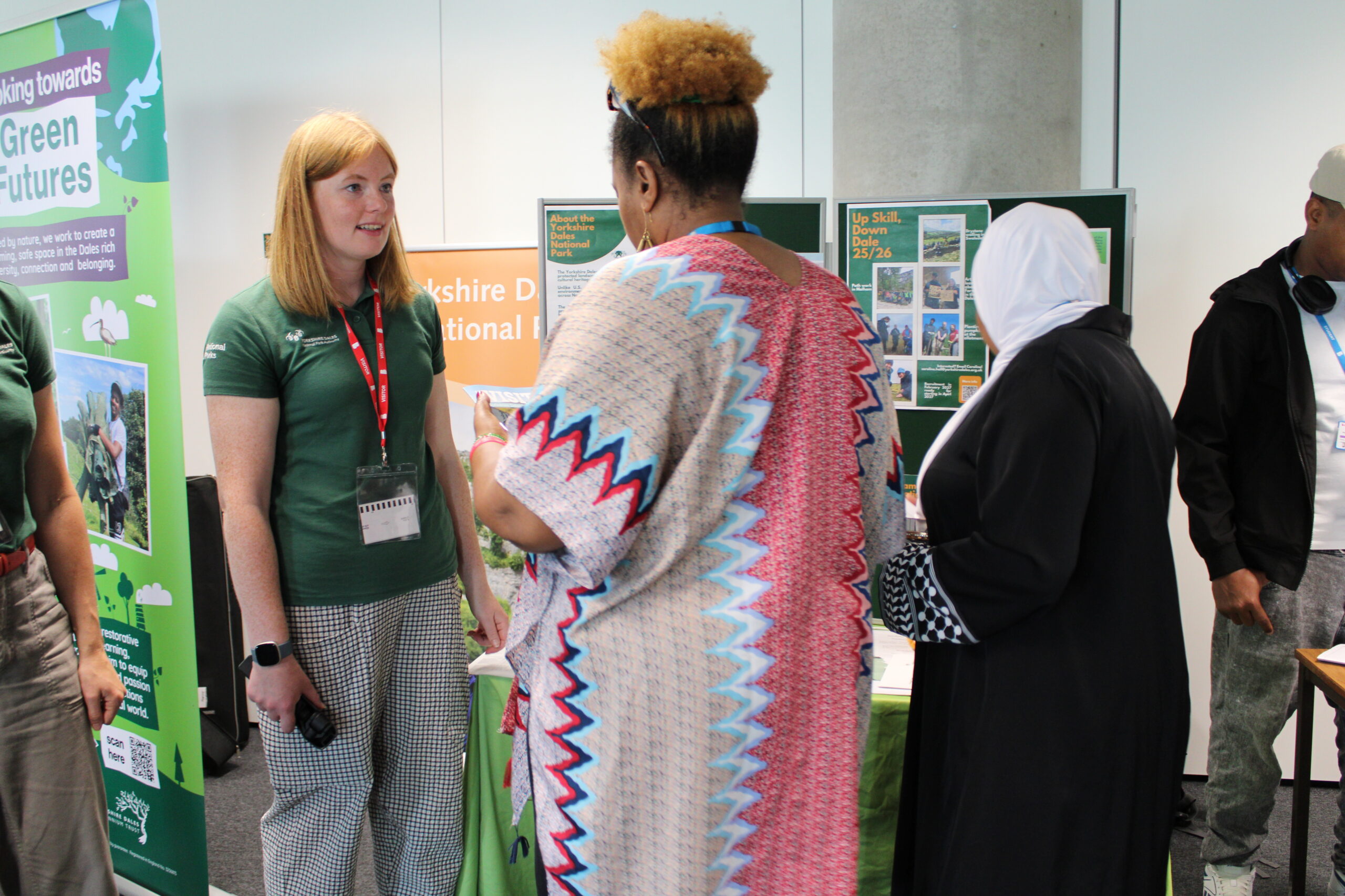 Two women stand in front of a table and display talking.