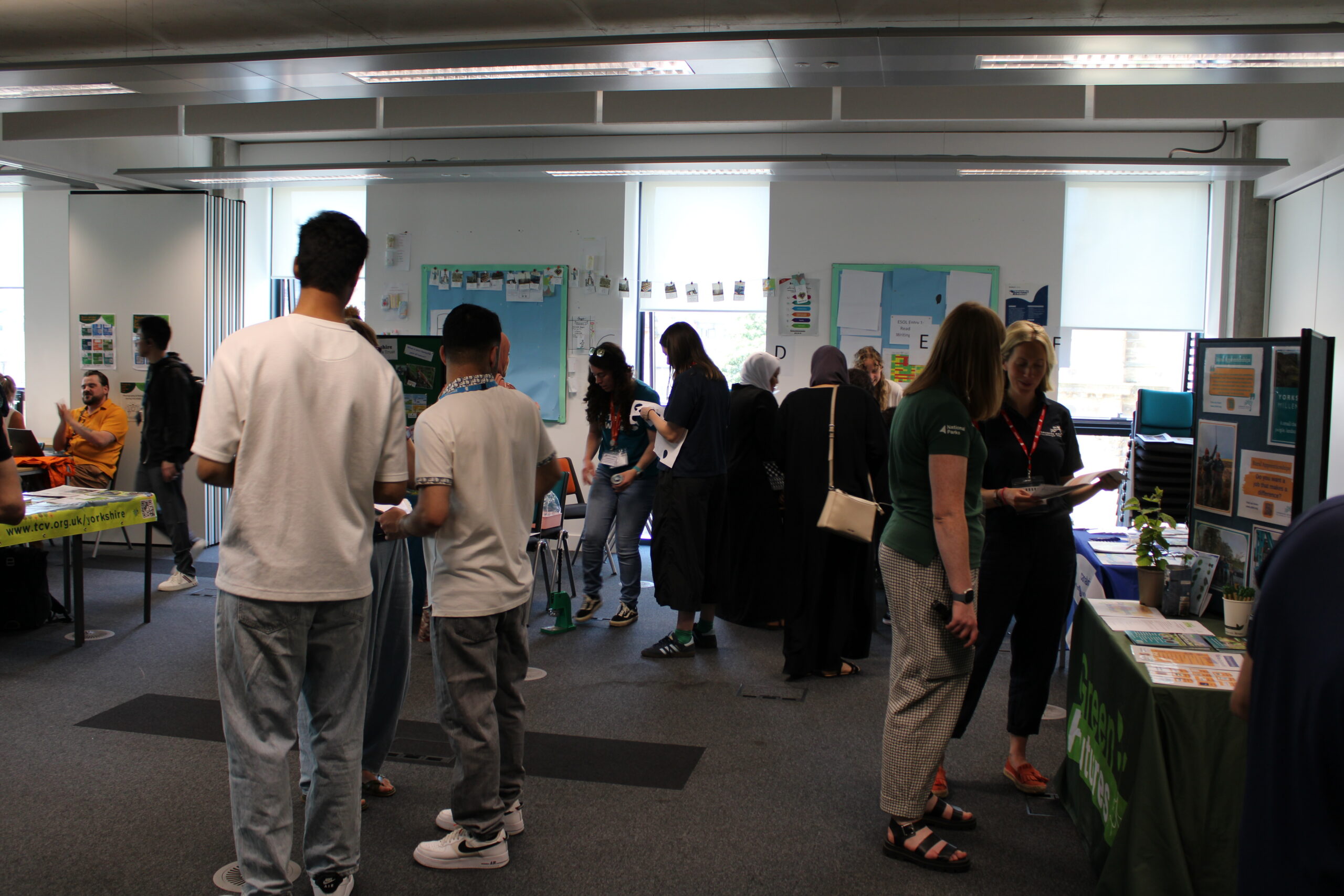 A large group of people stand in a room looking at stalls and talking to the visitors about volunteering opportunities.
