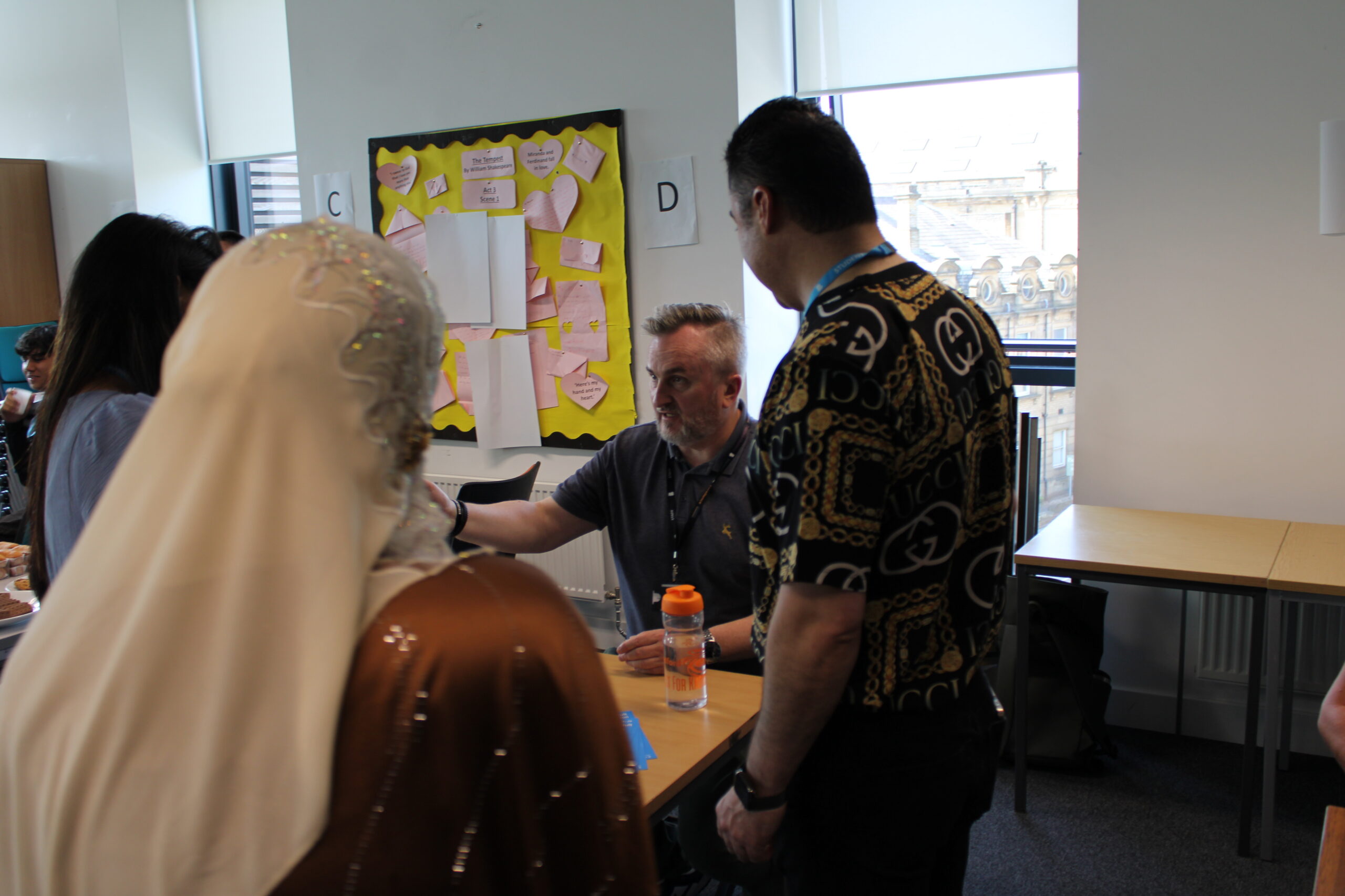 A group of people stand in front of a table and display talking together.